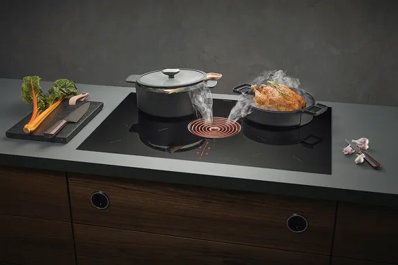 Schwarzes Induktionskochfeld von BORA mit integriertem Abzug, der Dampf von einem gebratenen Hähnchen absaugt.